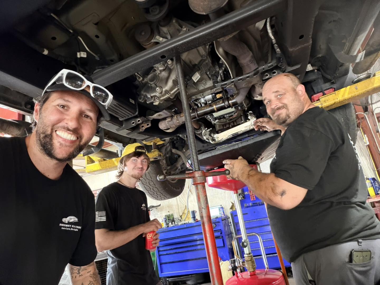 Three Broadway Auto Care team members servicing a vehicle on a lift